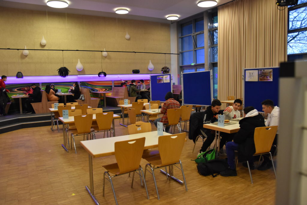 Mensa mit Tischen und Stühlen und bunter Beleuchtung.
